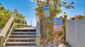 A wooden staircase leading to a beach area with signs indicating rip currents, dog-friendly beach access, and an unattended dog is prohibited on the beach from sunrise to sunset.