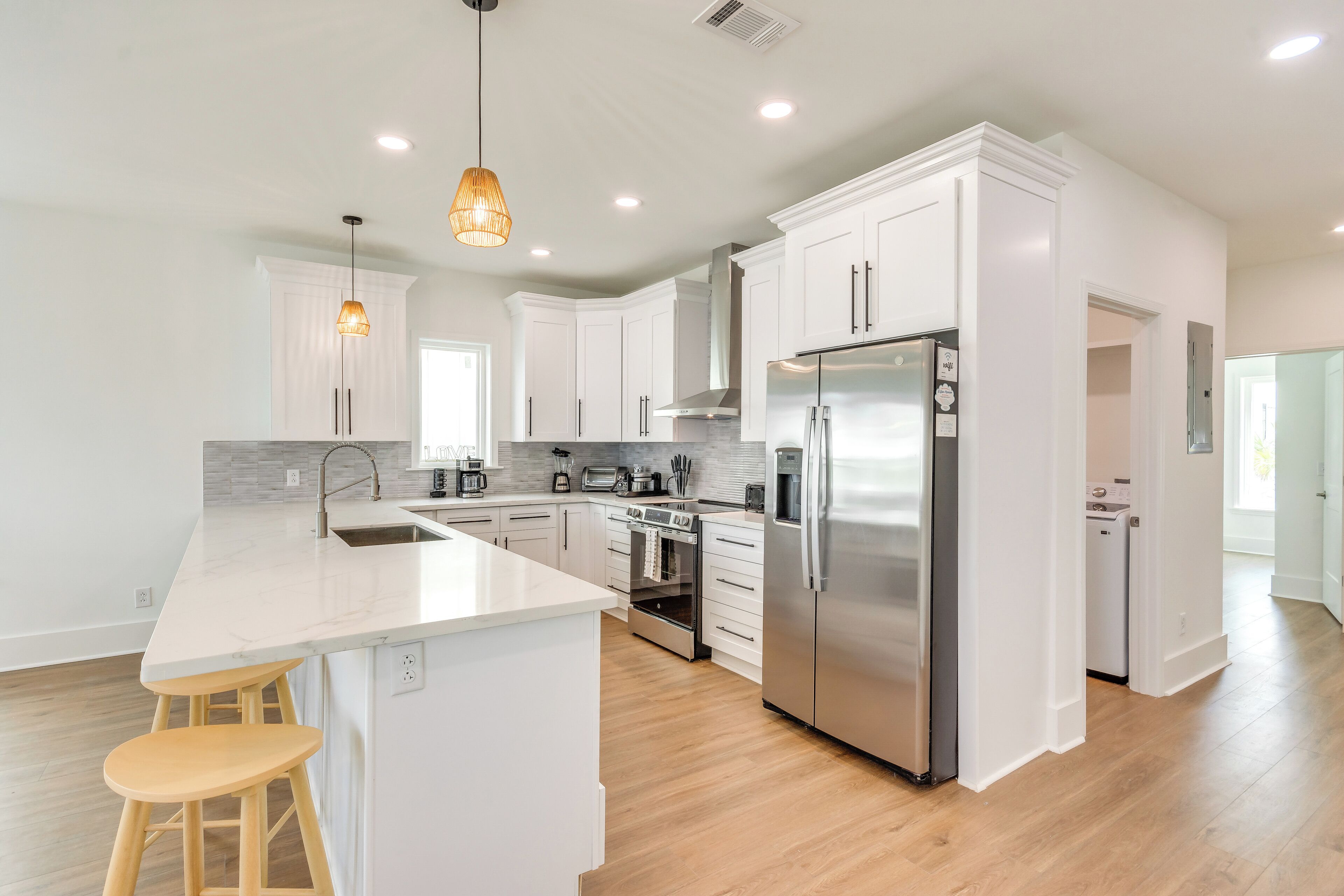 A modern kitchen with white cabinets, stainless steel appliances, a marble countertop, and wooden stools.