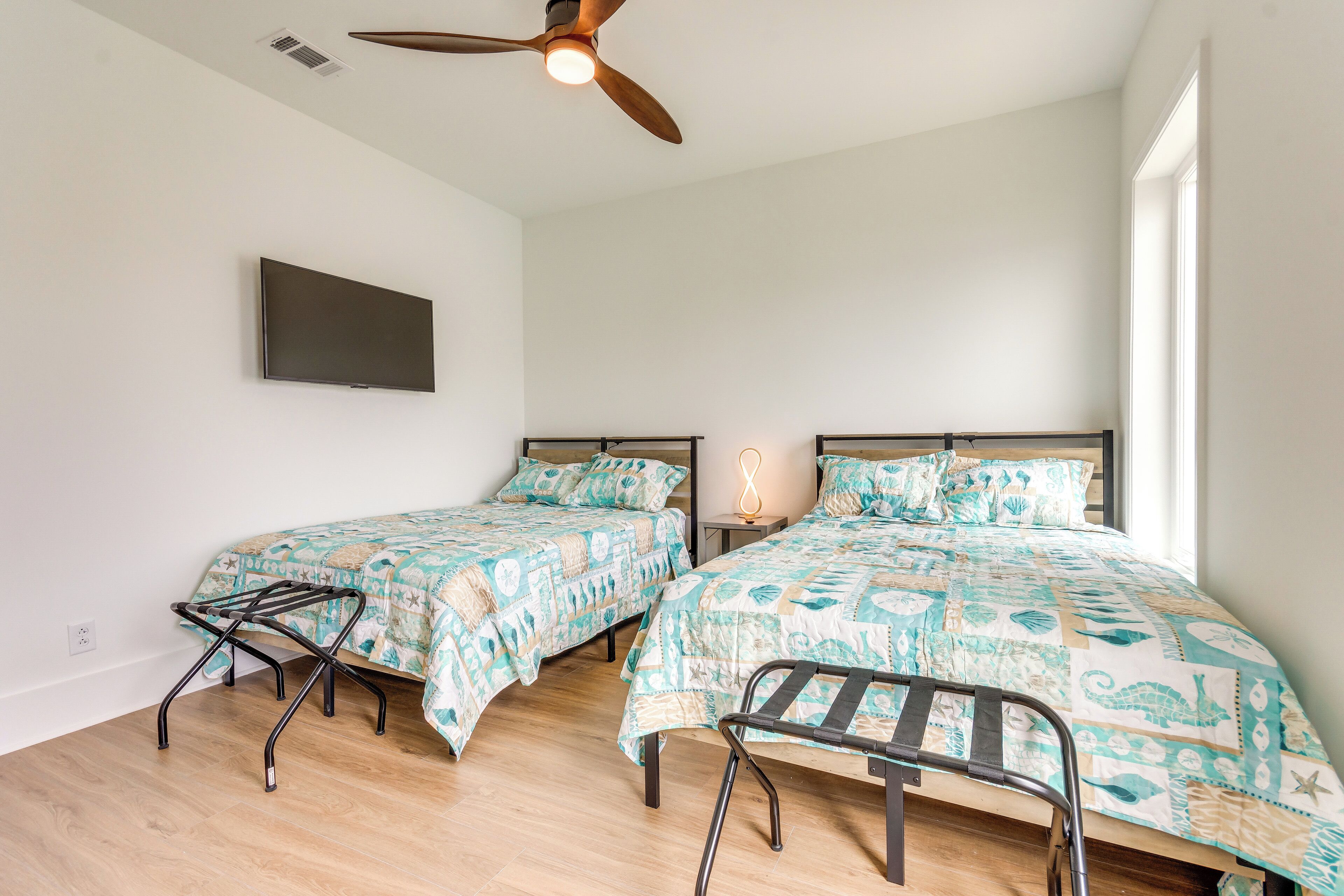 A bedroom with two beds, a ceiling fan, a TV, and a window.