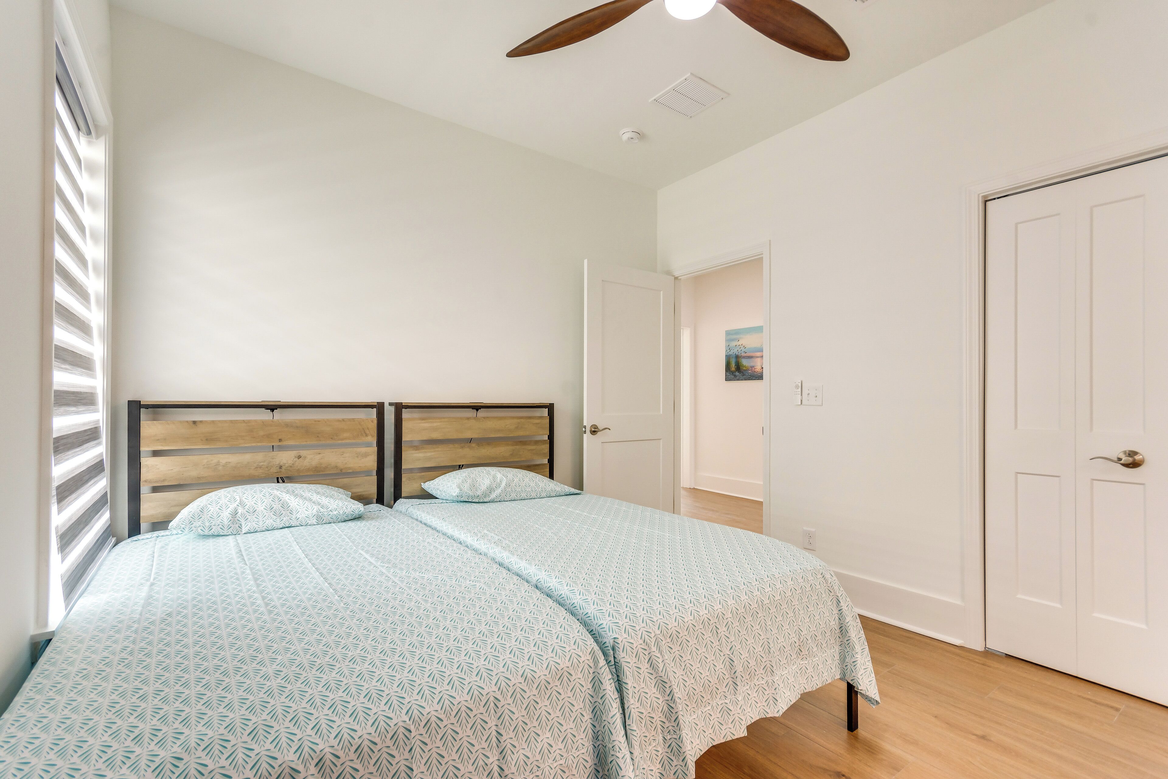 A bedroom with a wooden headboard, a bed with patterned bedding, a ceiling fan, and white doors.