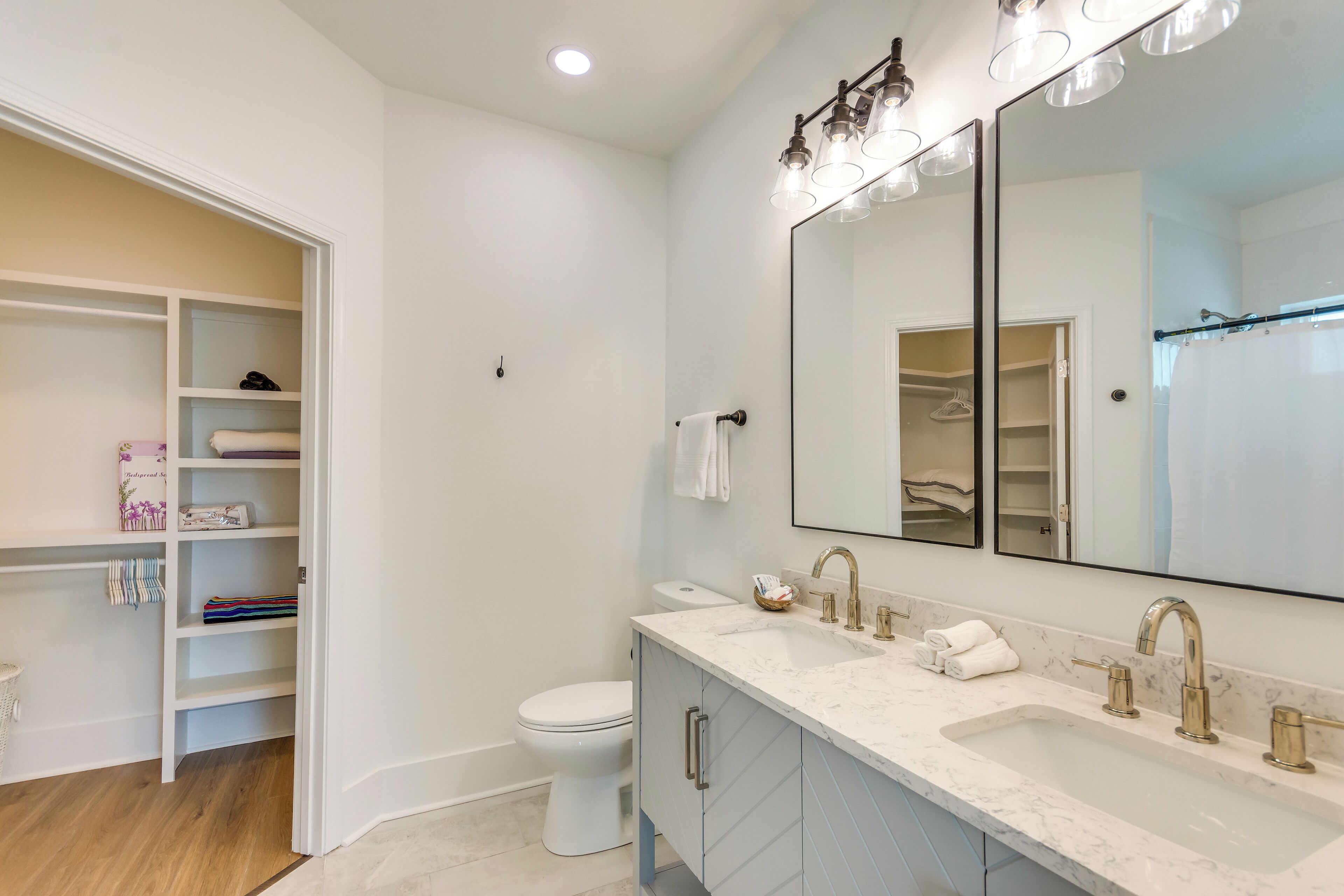 A modern bathroom with a large mirror, two sinks, and a walk-in closet.