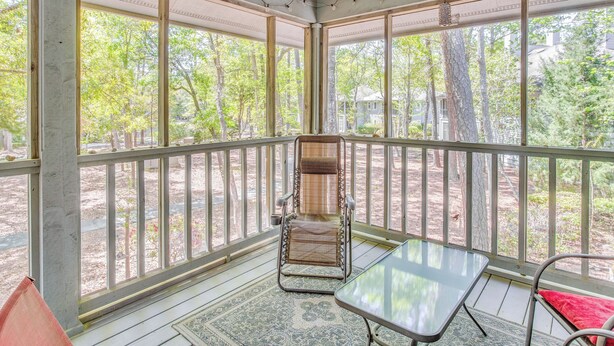 A covered porch with a cushioned chair, a small table, and a view of trees and a house in the background. - 3 Mi to Cherry Grove Beach: Coastal Condo Retreat! (North Myrtle Beach)