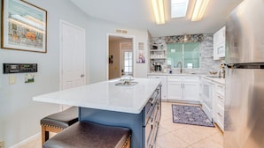 Cocina moderna con una isla de mármol, armarios blancos y un refrigerador de acero inoxidable.