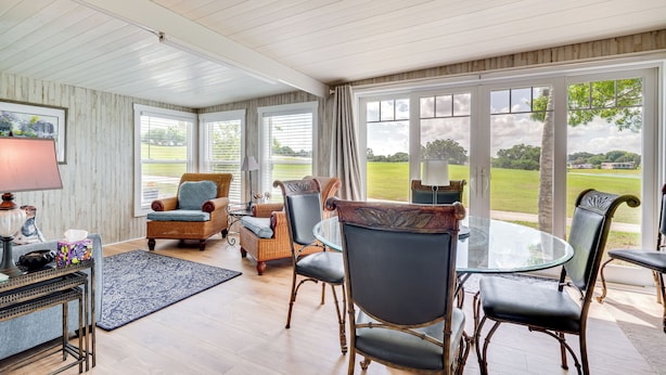 Una habitación amplia con una mesa de vidrio grande, asientos cómodos y ventanas grandes que ofrecen vistas a un paisaje verde.
