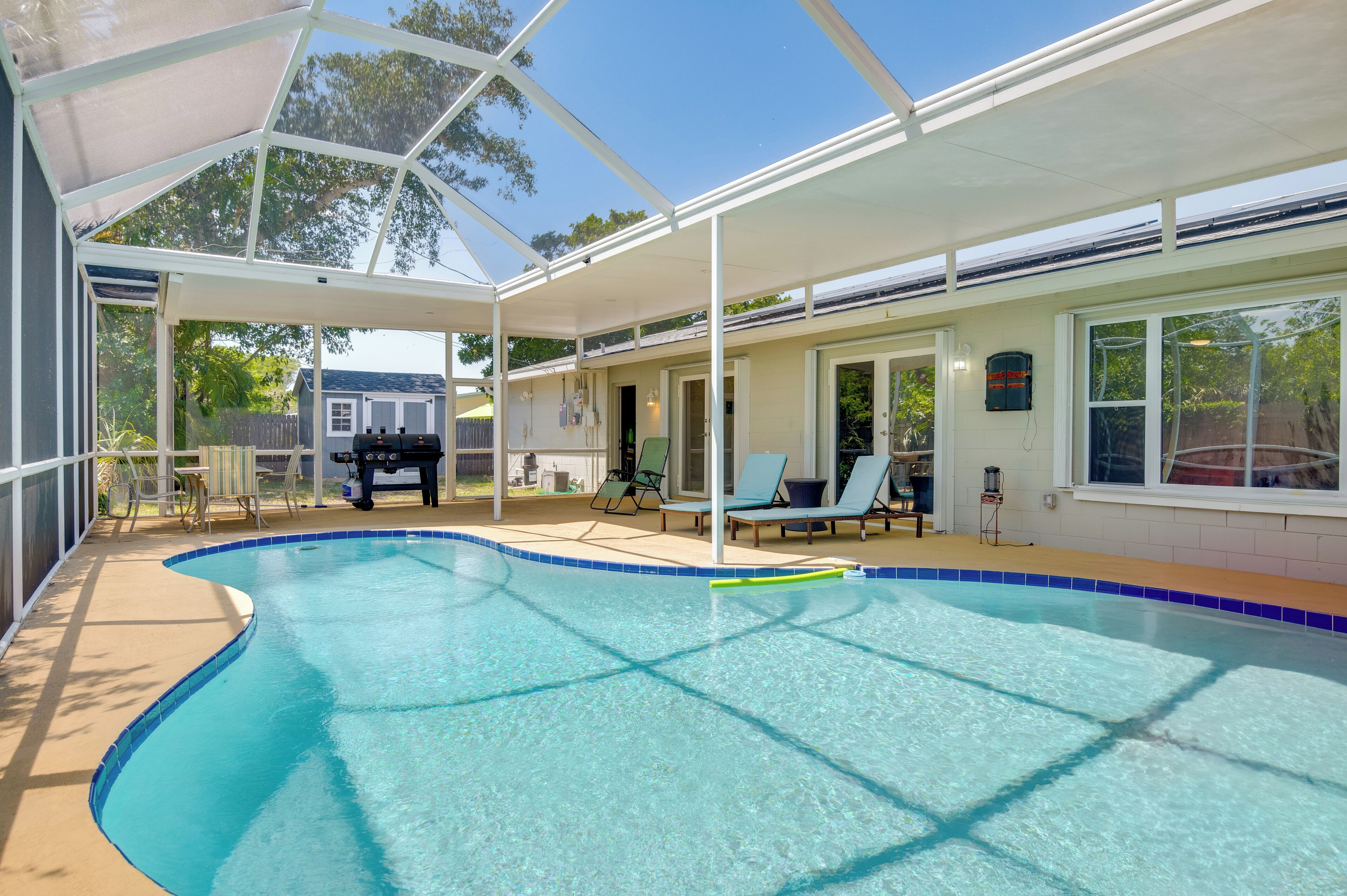A covered swimming pool with lounge chairs and a barbecue area.