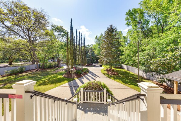 A residential driveway leading to a house with a white fence, a staircase, and a well-maintained lawn with trees and shrubs.