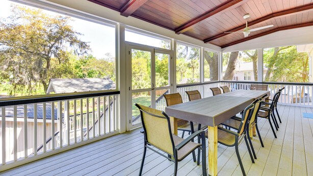 A covered outdoor deck with a wooden table and chairs, large windows, and a view of trees and a house. - 5 Mi to Beach: Spacious Home on Hilton Head Island (Hilton Head Island)