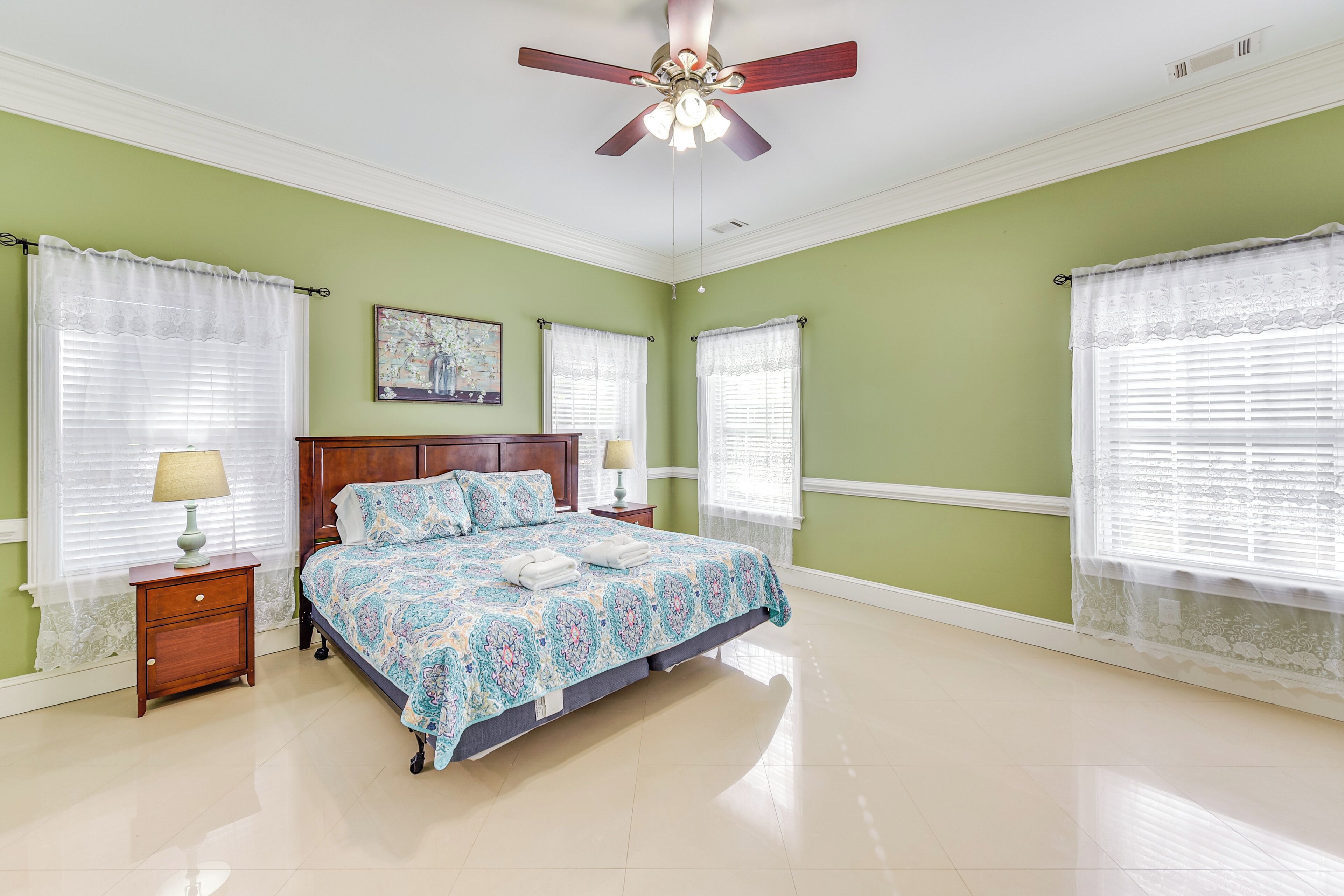 A bedroom with a bed, nightstands, a ceiling fan, and windows with curtains.