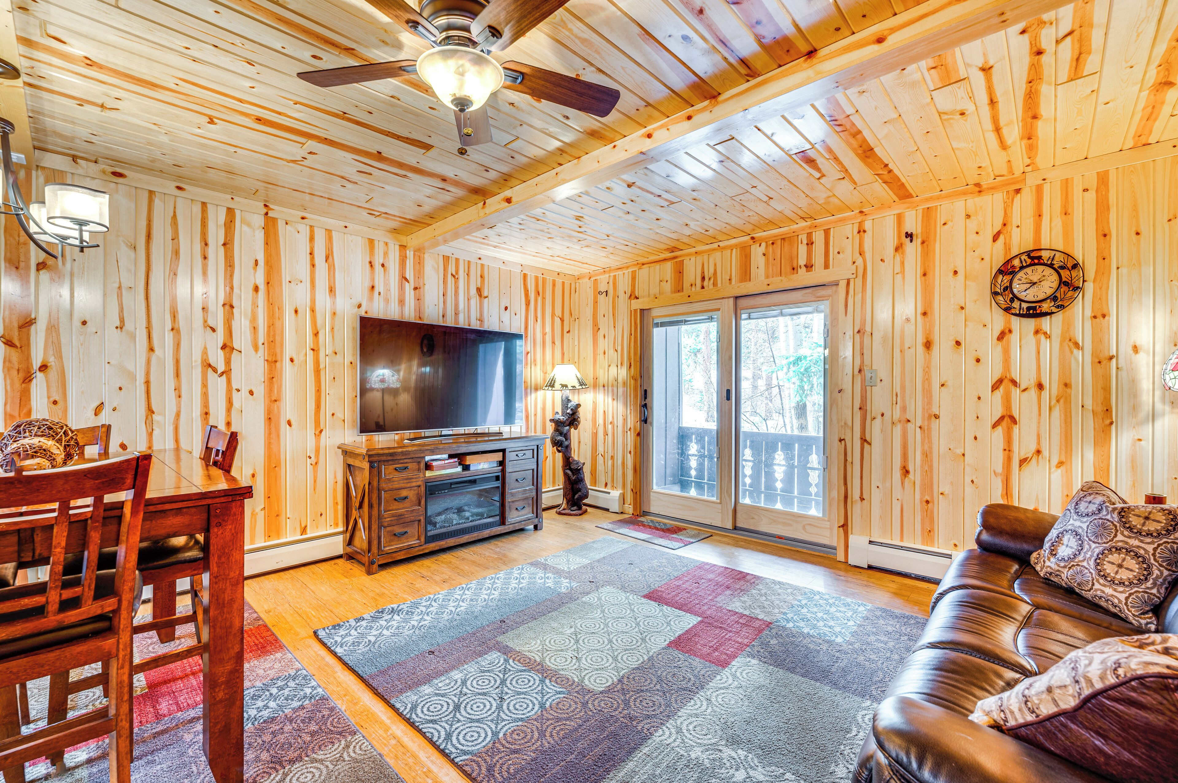 A wooden-paneled room with a television, a sofa, a dining table, and a ceiling fan.