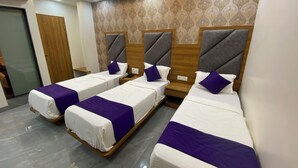 Une chambre d’hôtel avec trois lits simples, chacun doté d’une tête de lit en bois et d’un coussin décoratif de couleur violette.