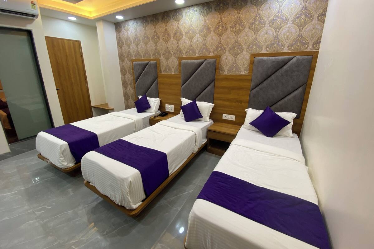 A hotel room with three single beds, each with a wooden headboard and a purple accent pillow.