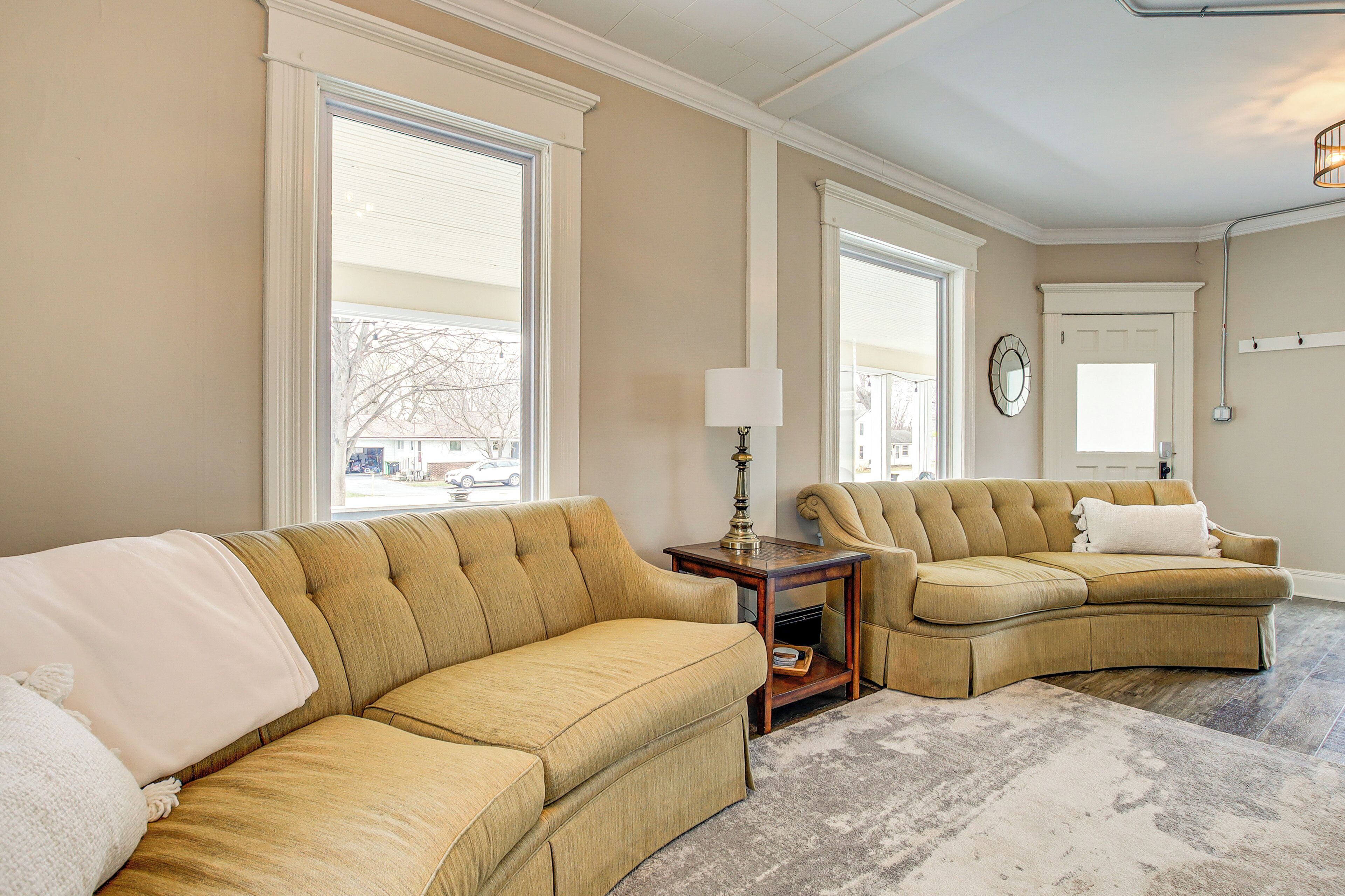 Una sala de estar con dos sofás color beige, una pequeña mesita de madera y un ventanal con contraventanas blancas.