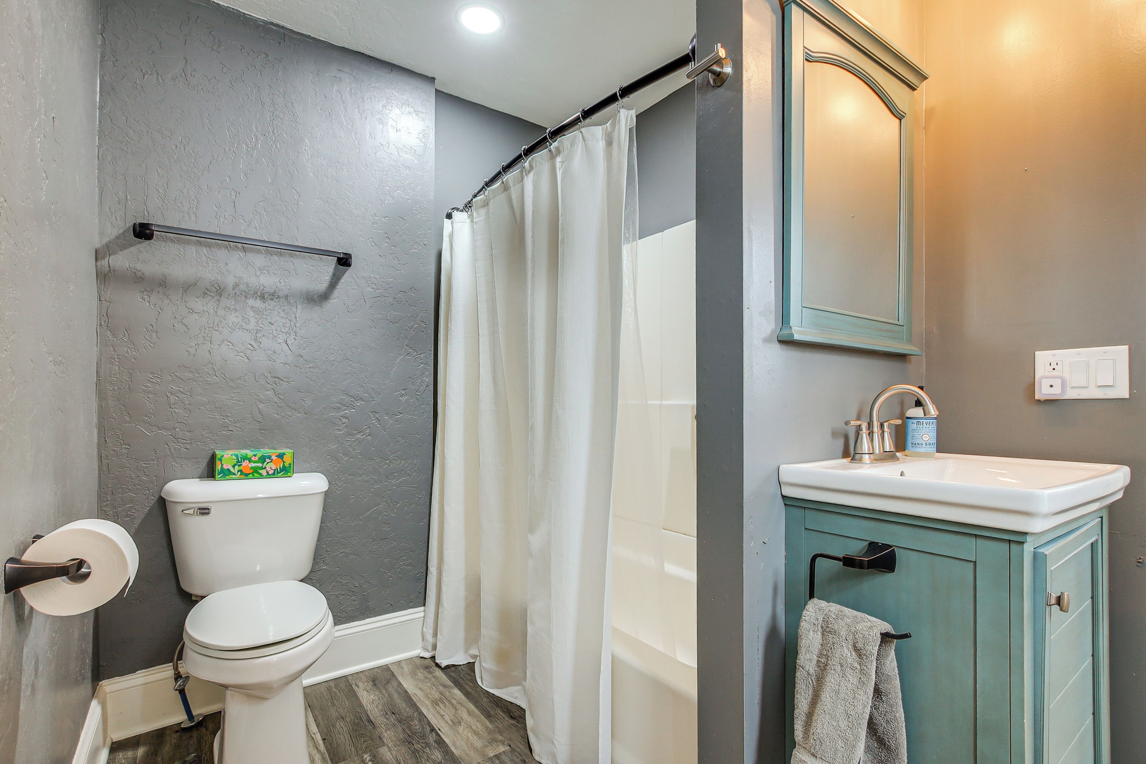 Une salle de bain équipée de toilettes, d’un rideau de douche, d’un lavabo et d’un meuble de rangement.