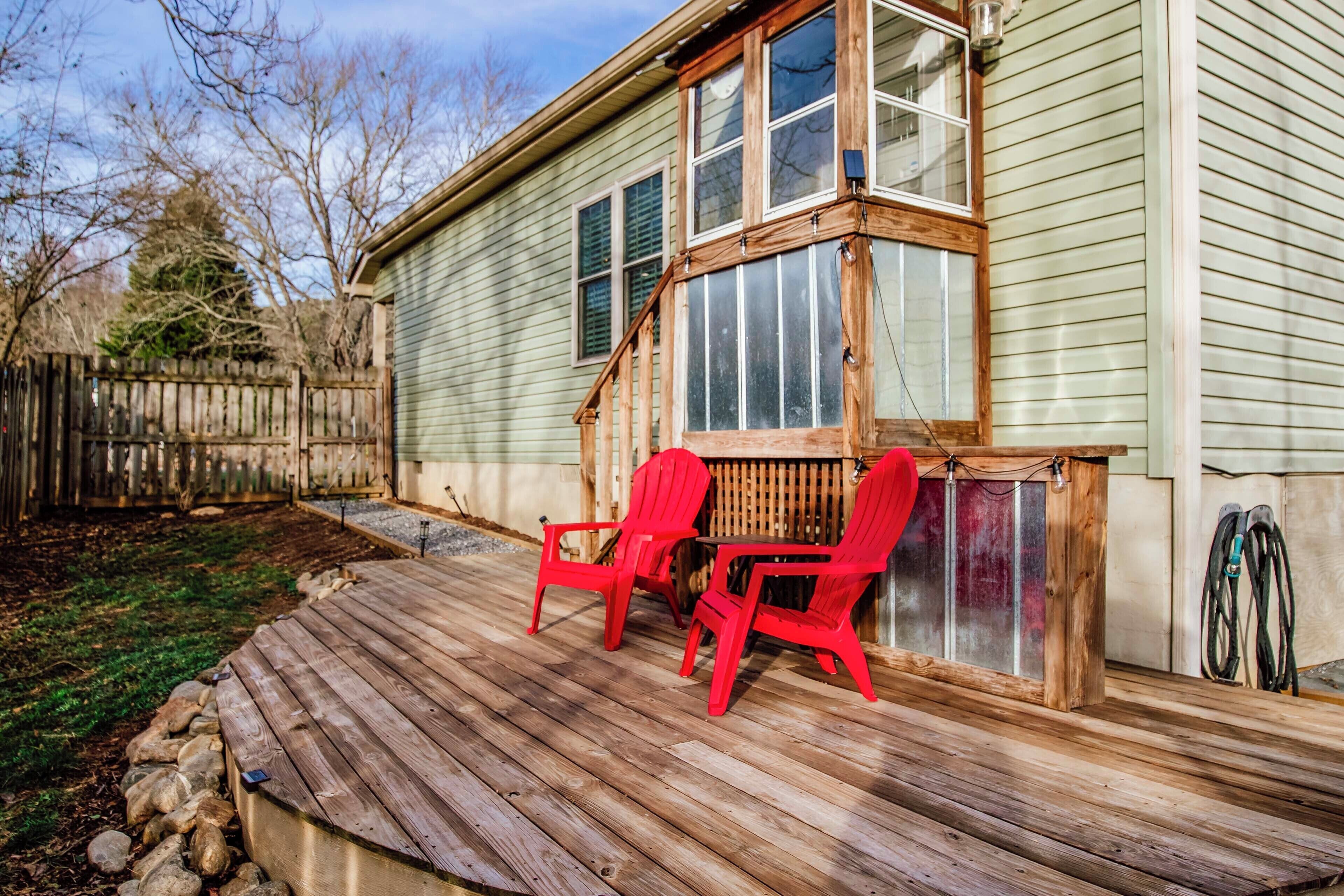 A wooden deck with two red chairs and a grill area.