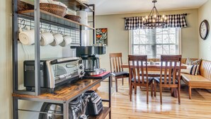 A kitchen with a coffee machine, toaster, and shelves with mugs and baskets. There is a dining table with chairs and a sofa in the living area. - 1 Mi to Dtwn Black Mountain: Home w/ Patio & Yard (Black Mountain)