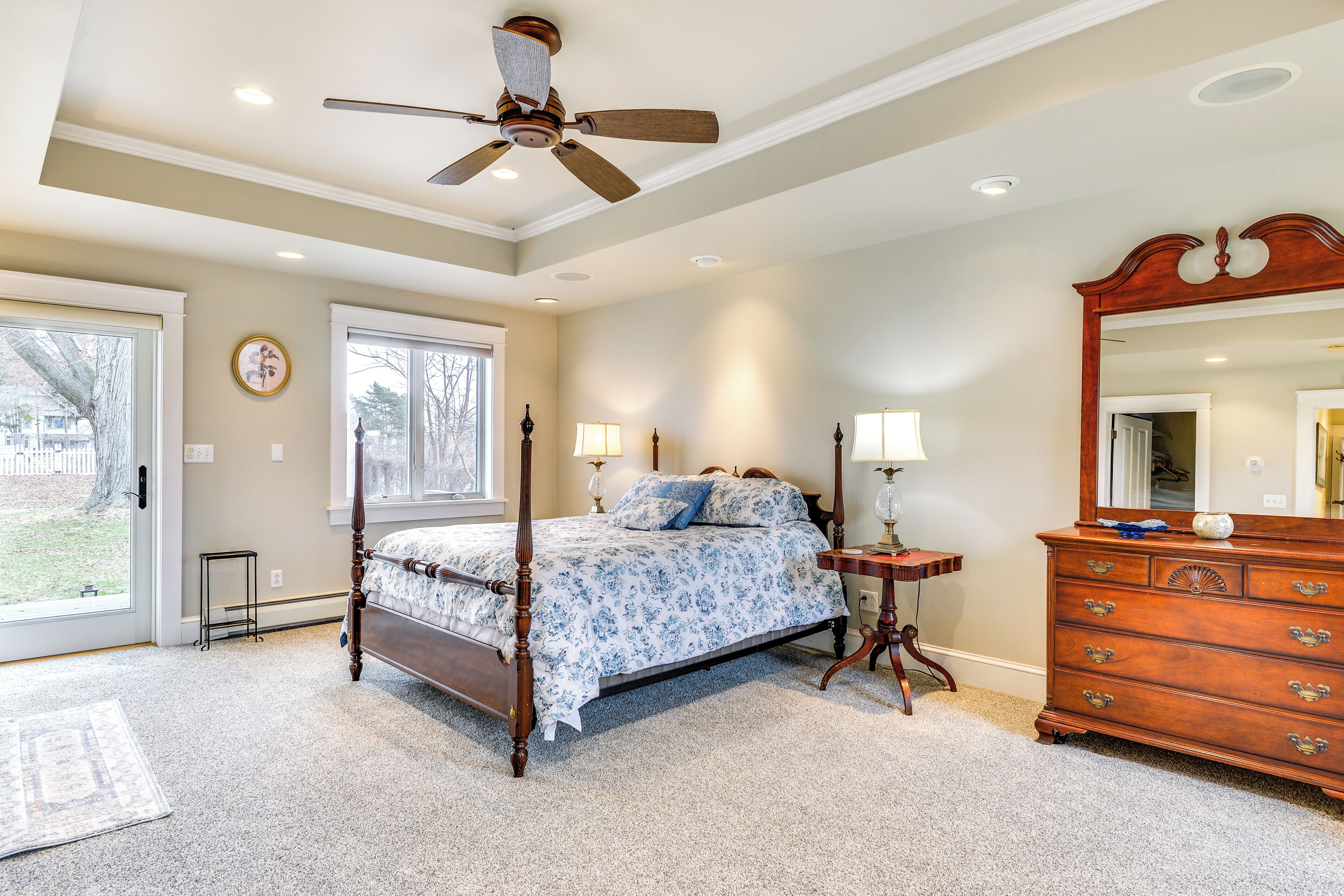 A four-poster bed with a wooden headboard, a dresser with drawers, and a ceiling fan.
