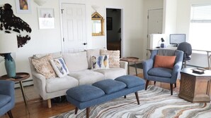 Un salon comprenant un canapé, un fauteuil bleu, un pouf et un tapis à motifs.
