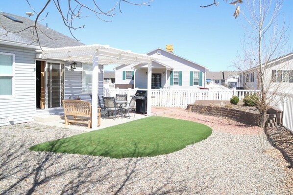 A residential backyard with a patio, a grill, and a small lawn.