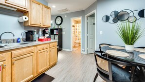 A modern kitchen with wooden cabinets, a built-in coffee maker, and a dining area with a round table and chairs. - Near Speedway & Shops: Concord Apt w/ Shared Yard! (Concord)