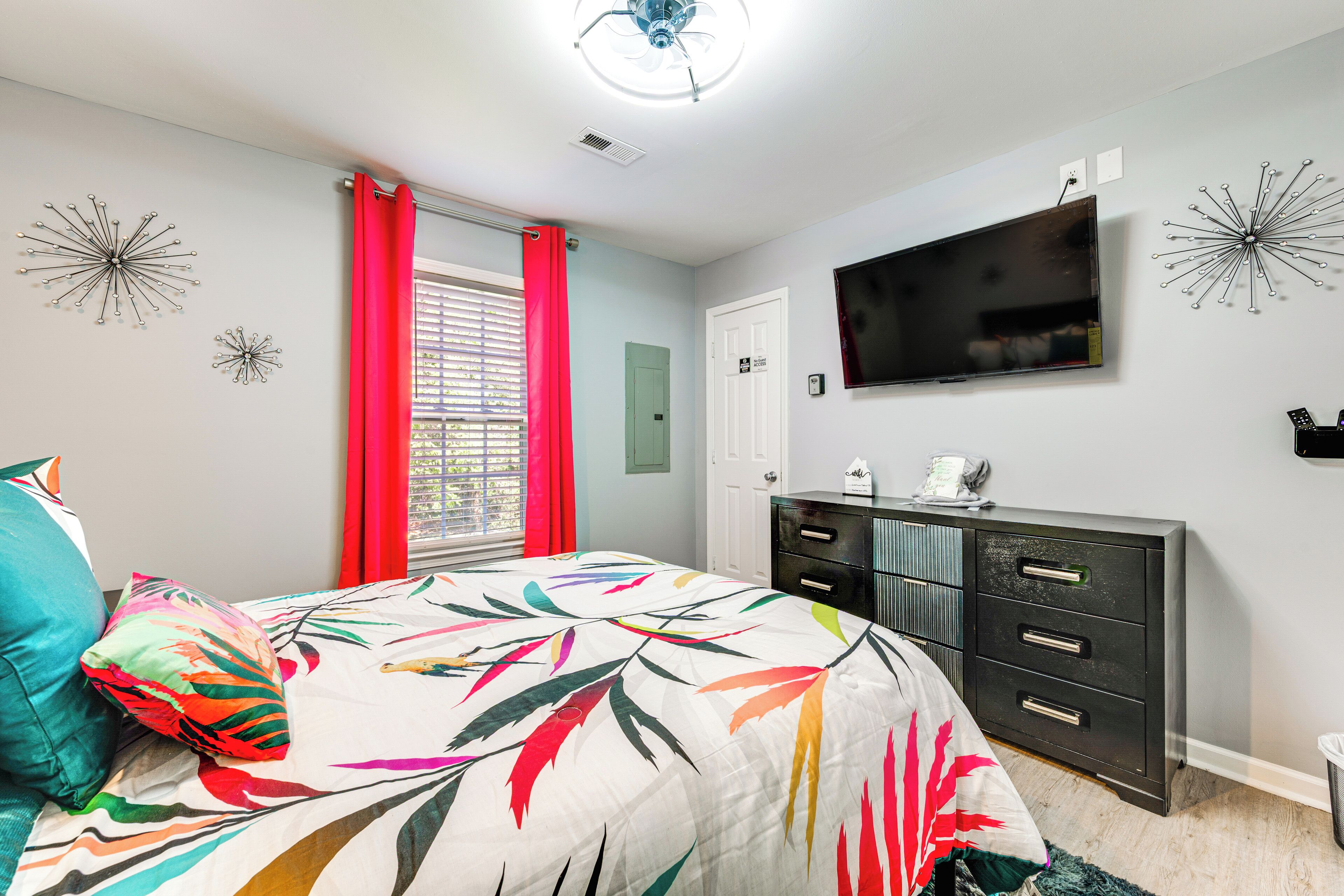 A bedroom with a bed, a dresser, a television, and decorative wall art.