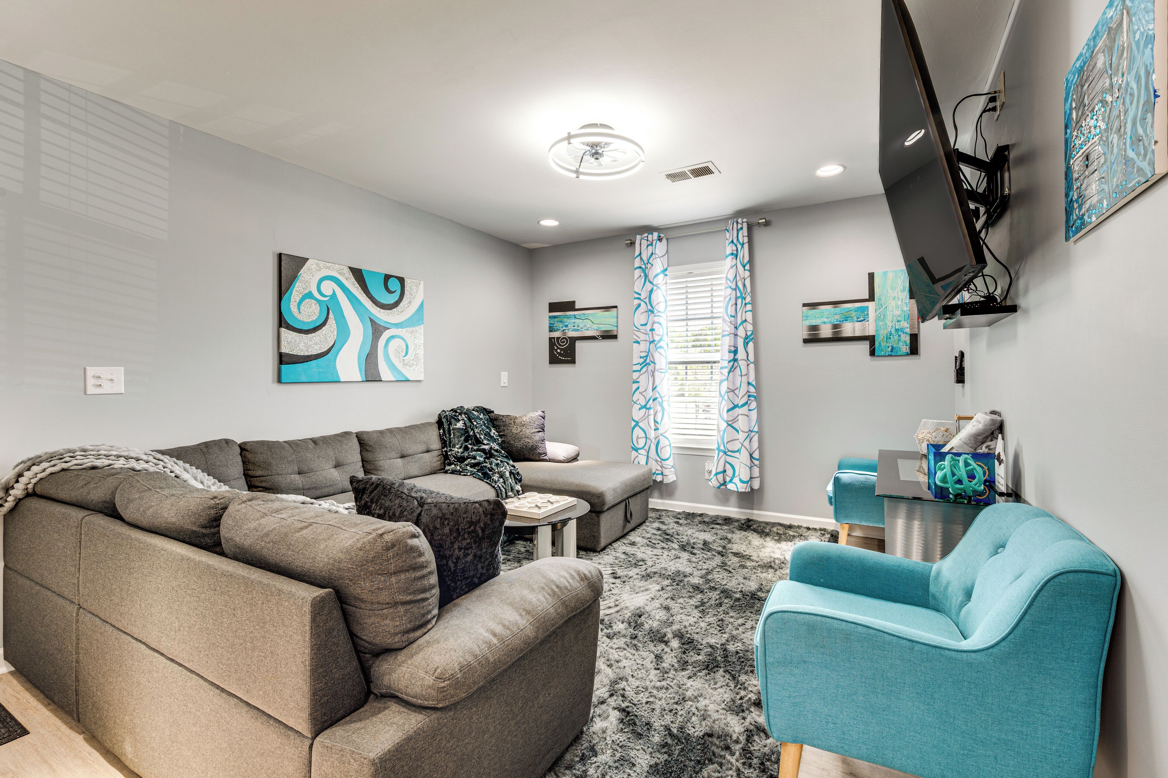 Un salon moderne avec un canapé d’angle, un fauteuil turquoise et des œuvres d’art abstraites accrochées au mur.