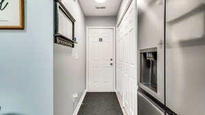 A hallway with a white door, a black doormat, a stainless steel refrigerator, and a framed picture on the wall. - Near Speedway & Shops: Concord Apt w/ Shared Yard! (Concord)