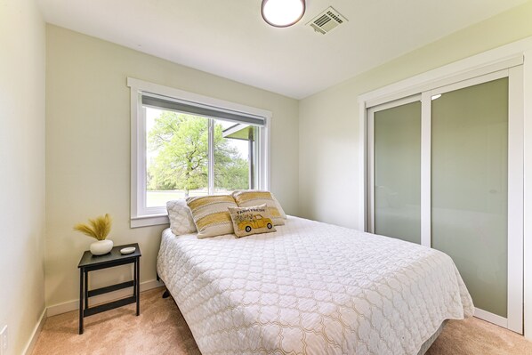 A bedroom with a bed, a nightstand, a window, and a sliding door. - 5 Mi to Lake Texoma: Wooded Retreat on 3 Acres! (Tishomingo)