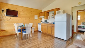 Una cocina compacta con armarios de madera, un refrigerador blanco y un comedor con sillas y una mesa blancos.