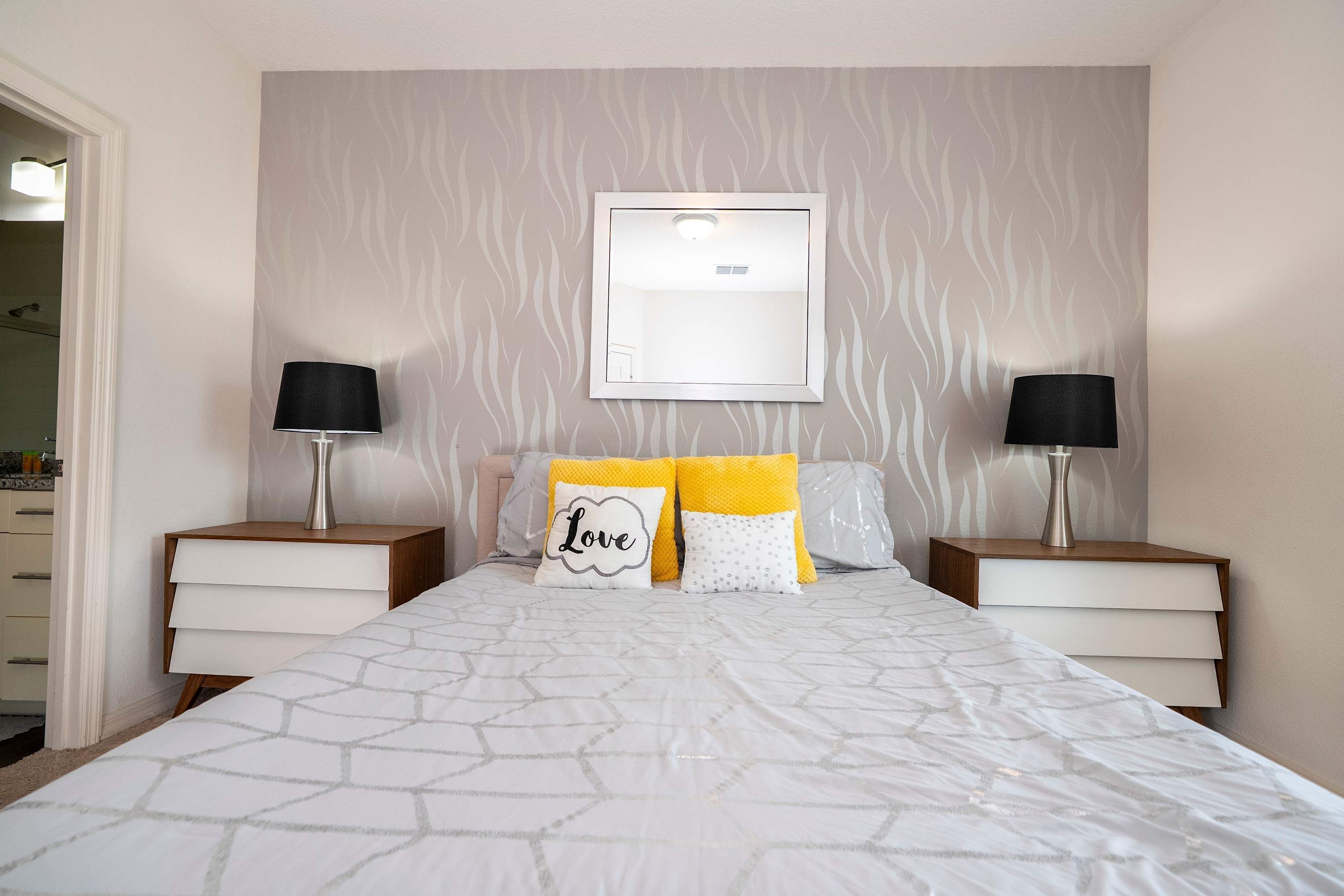 Une chambre à coucher bien rangée, avec un lit, deux tables de chevet, une lampe fixée au mur et un tableau encadré au-dessus du lit.