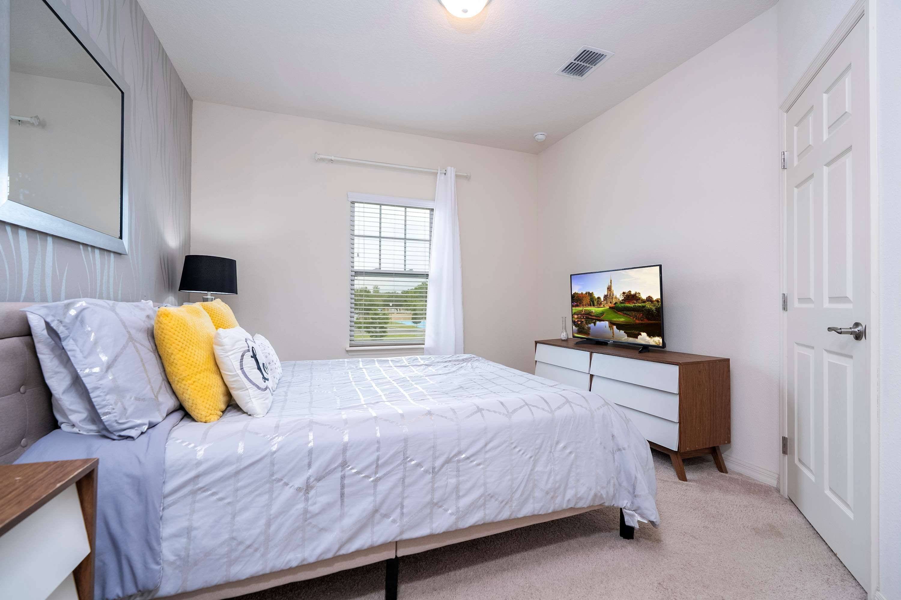 A bedroom with a bed, a dresser, a television, and a window with blinds.