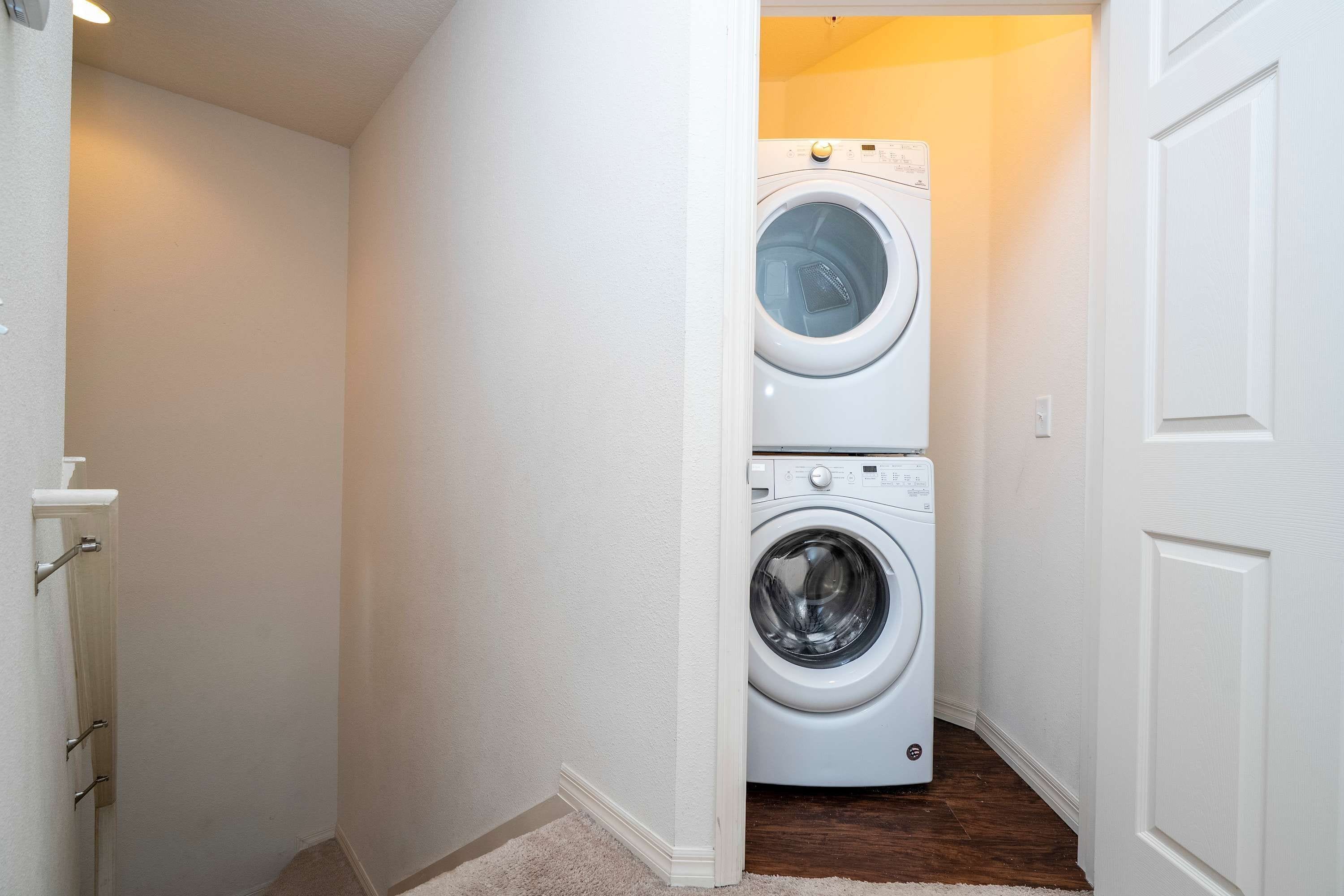 A laundry room with a front-loading washer and dryer, wooden flooring, and white walls.