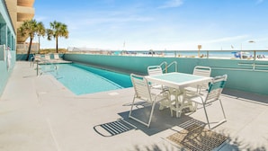 Un espace aménagé au bord de la piscine, avec vue sur la plage, comprenant des chaises longues et une table.