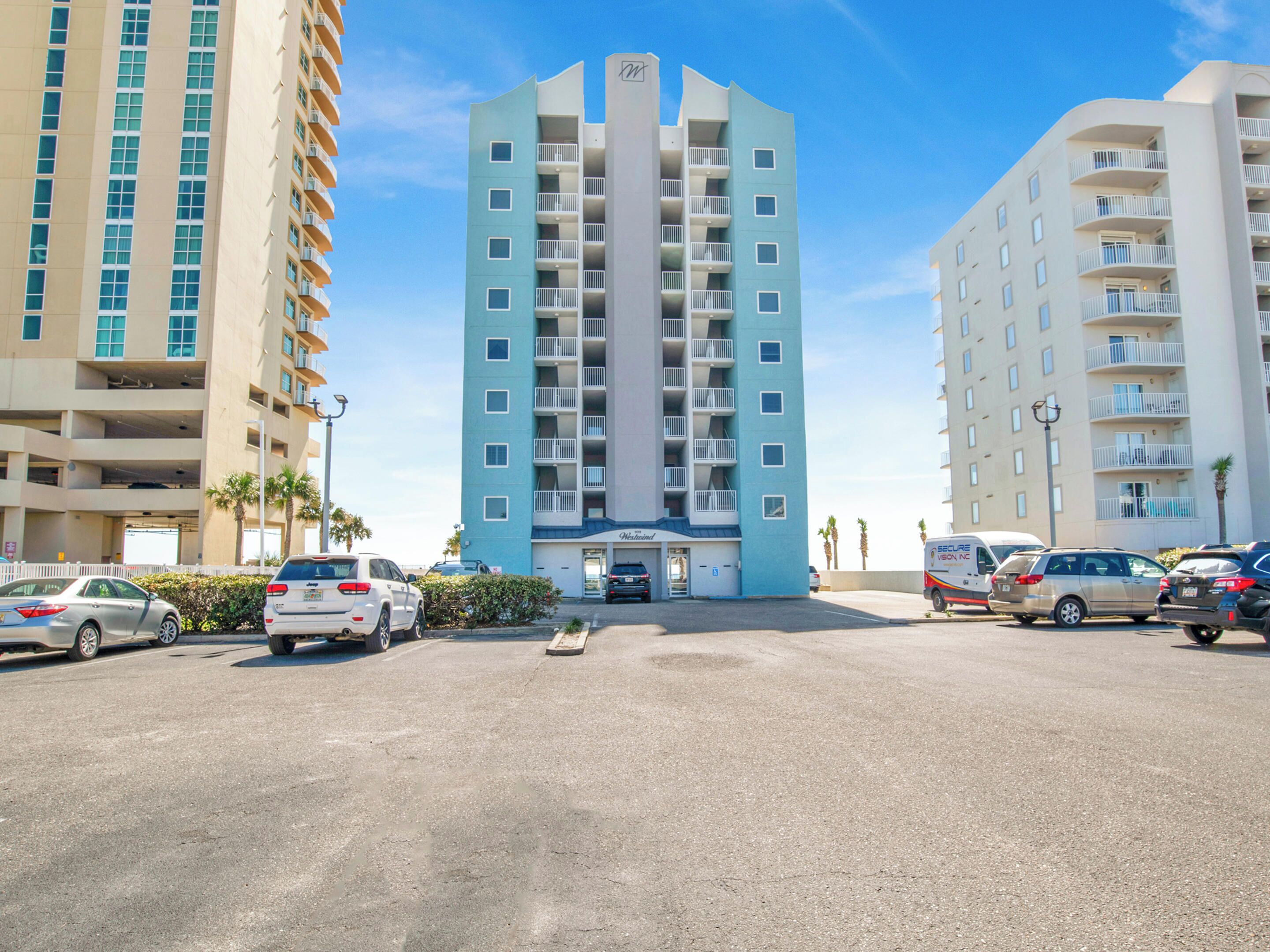 A multi-story hotel with a central entrance, parking lot, and surrounding buildings.