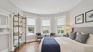 Une chambre avec un grand lit, une étagère en verre, deux chaises, une petite table et une fenêtre donnant sur un beau paysage.