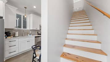 Une cuisine moderne avec des meubles blancs, un escalier en bois et un coin repas équipé d’une chaise.