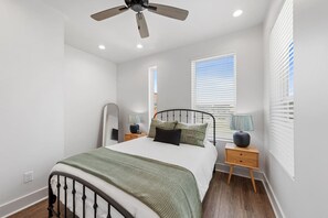 Une chambre à coucher comprenant un lit, des tables de chevet, un ventilateur de plafond et des fenêtres équipées de stores.