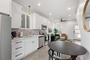Une cuisine moderne avec des meubles blancs, un coin repas doté d’une table ronde et un ventilateur de plafond.
