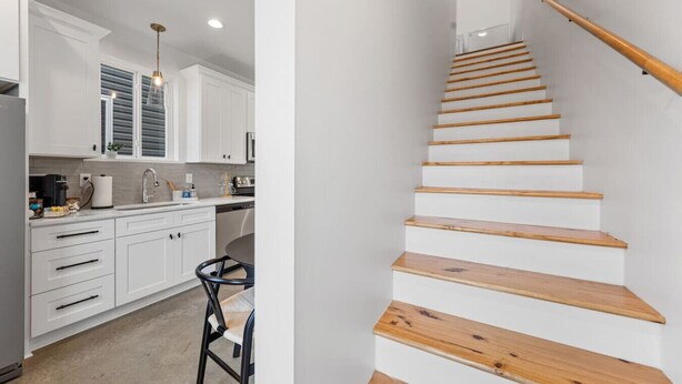 Une cuisine moderne avec des meubles blancs, un escalier en bois et un coin repas équipé d’une chaise.