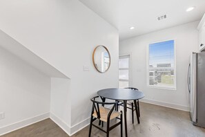 Une cuisine moderne avec des murs blancs, une table ronde, deux chaises, un réfrigérateur et une fenêtre avec des stores.