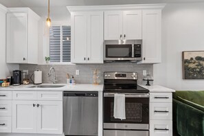 Cocina moderna con armarios blancos, microondas de acero inoxidable, horno, lavavajillas y una silla tapizada de color verde.