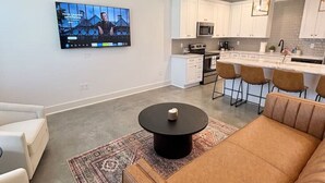 Moderni olohuone, jossa on ruskea sohva, pyöreä sohvapöytä ja seinälle asennettu televisio.