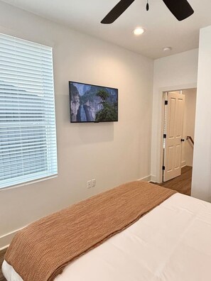 Une chambre à coucher avec un lit, un téléviseur fixé au mur et une fenêtre avec des stores.