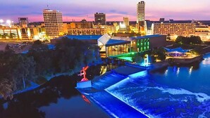 Un hôtel situé au bord de l’eau, doté d’un élément décoratif aquatique, de bâtiments illuminés et offrant une vue sur le panorama urbain en arrière-plan.