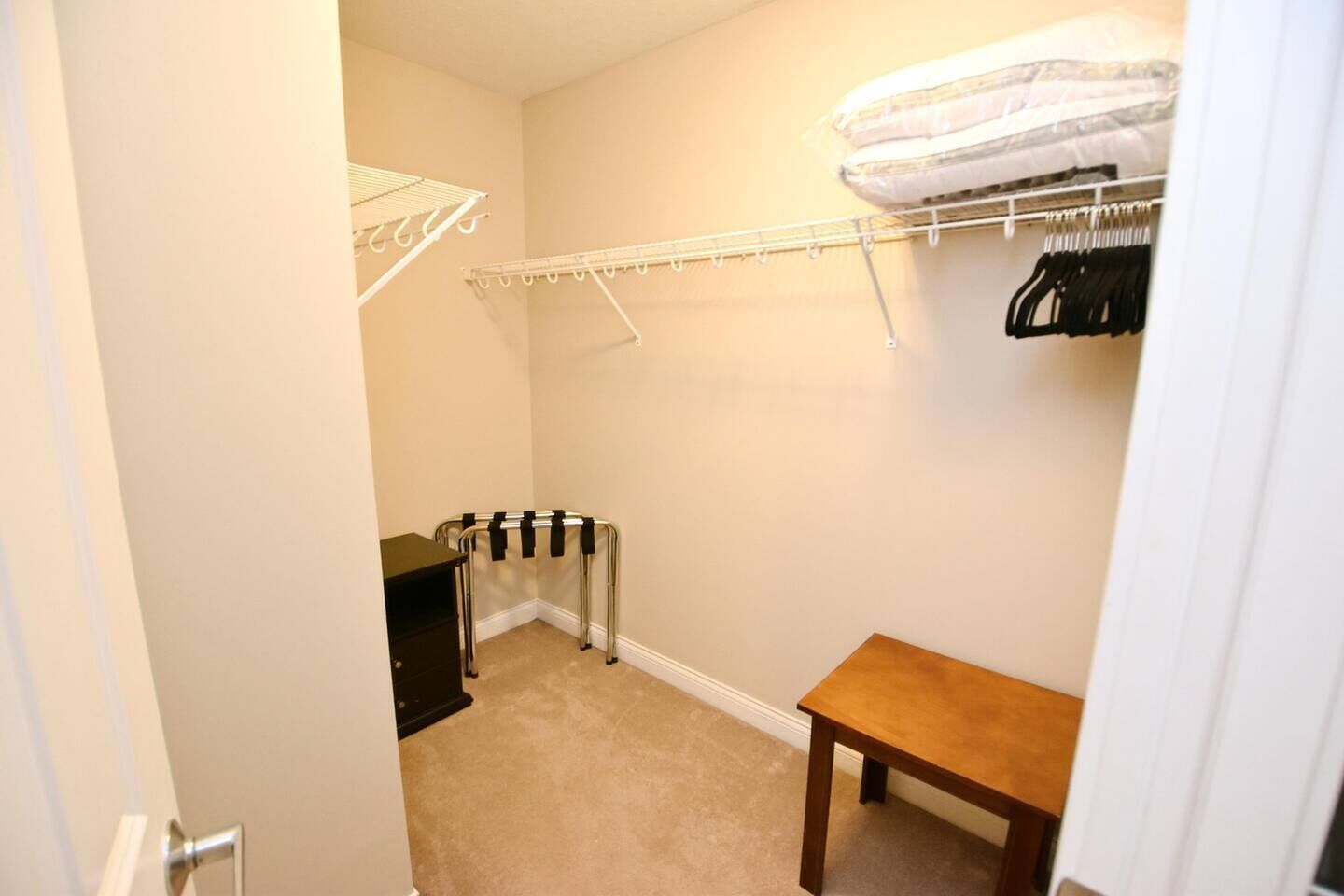 Ein kleines Zimmer mit Holztisch, Heizkörper, weißer Wand und Schrank mit Kleidung.