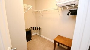 Une petite pièce avec une table en bois, un radiateur, un mur blanc et une armoire où sont suspendus des vêtements.