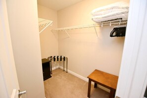 A small room with a wooden table, a radiator, a white wall, and a closet with hanging clothes.