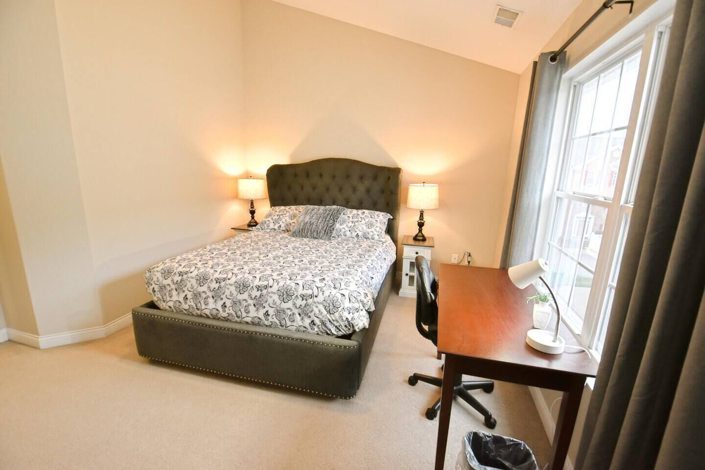 Une chambre à coucher avec un lit, des lampes de chevet, un bureau avec une chaise et une fenêtre.