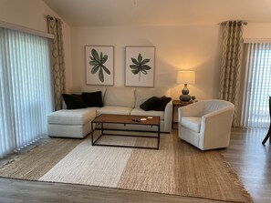 A living room with a sofa, armchair, coffee table, and two wall-mounted plant prints.