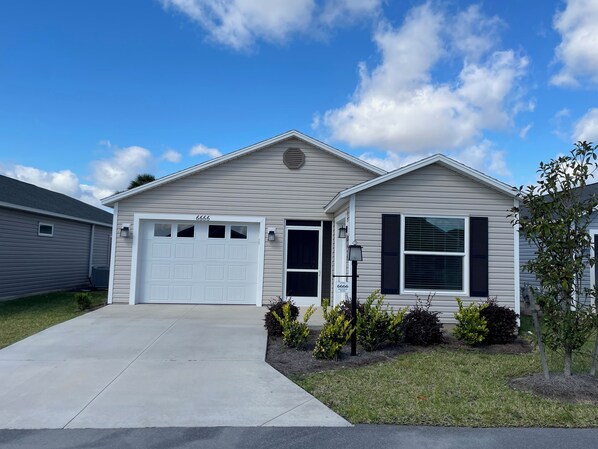 A single-story house with a white garage door, a small porch with a black lamp post, and a clear blue sky.