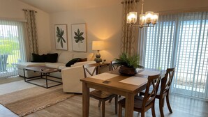 Ein modernes Wohnzimmer mit Essbereich, ausgestattet mit einer Couch, einem Couchtisch, einem Esstisch, Stühlen und einer Topfpflanze.